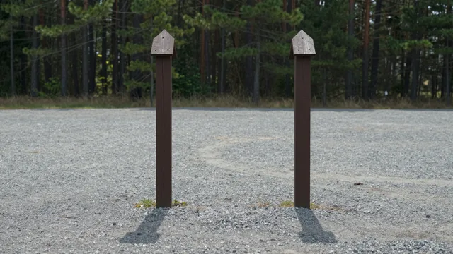 Two identical wooden campsite marker posts standing side by side in an empty gravel clearing — an illustration of one record counted twice, not a photograph of a place.