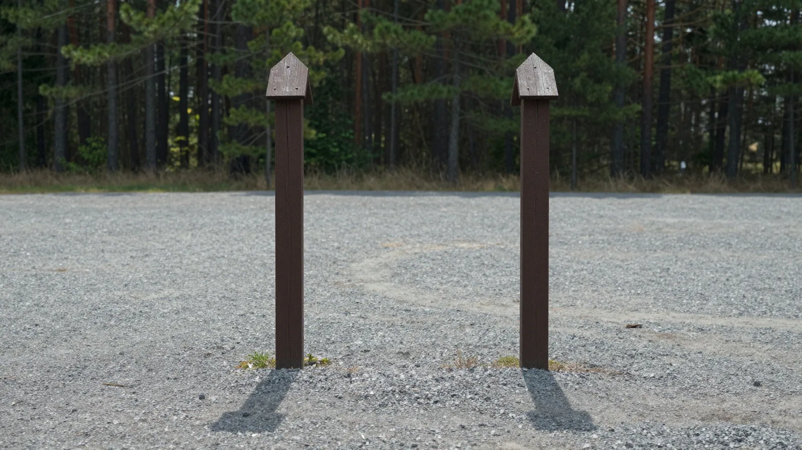 Two identical wooden campsite marker posts standing side by side in an empty gravel clearing — an illustration of one record counted twice, not a photograph of a place.