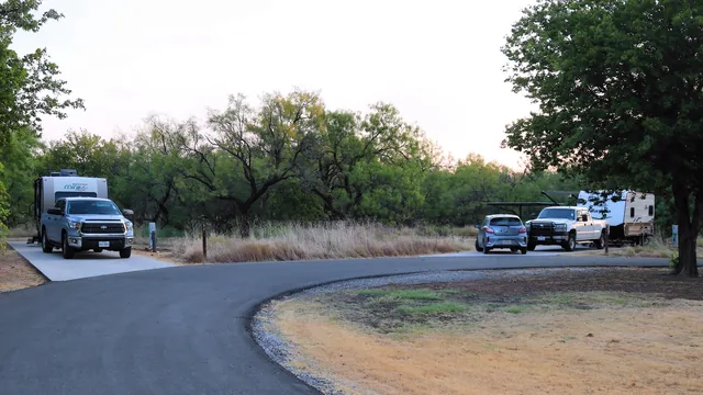 A paved campground loop at Lake Arrowhead State Park in Texas, a fifth wheel backed onto a pad on one side and travel trailers on the other.