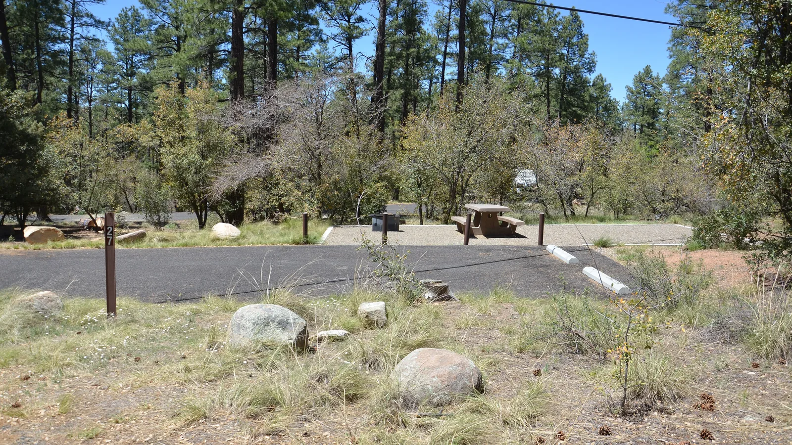 Campsite 27 at White Spar Campground in the Prescott National Forest: a paved driveway spur in the foreground, and beyond it the gravel pad holding the picnic table and fire ring.